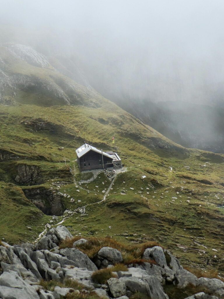 A solitary mountain hut surrounded by misty Swiss Alps landscape.